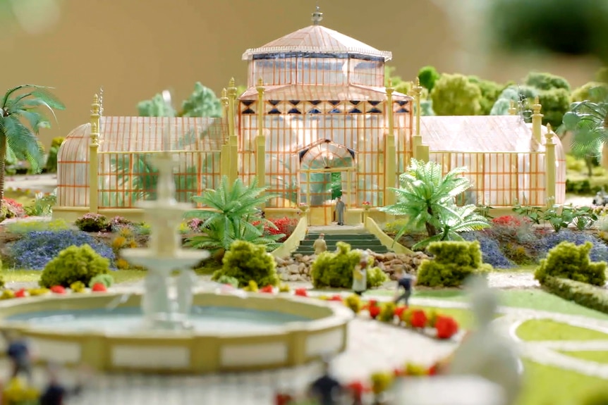 A model of a glass house with miniature plants and bird baths surrounding it
