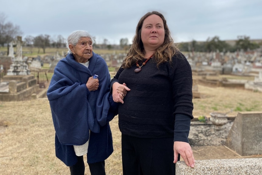 a woman holding the hand of an older woman while both standing at a cemetery