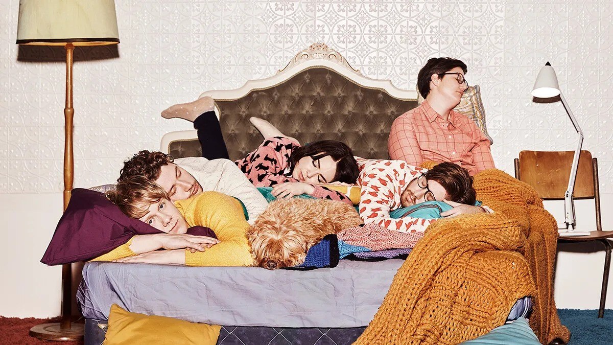 Josh Thomas, Keegan Joyce, Emma Barclay, Tom Ward and Hannah Gadbsy lie on a bed with a dog