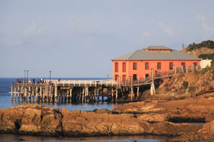 A small crowd of people gathered on a historic wooden wharf nestled among the rocks