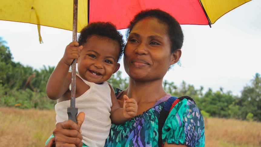 A woman holding a smiling baby under an umbrella