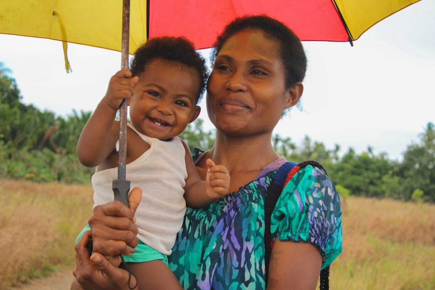 A woman holding a smiling baby under an umbrella