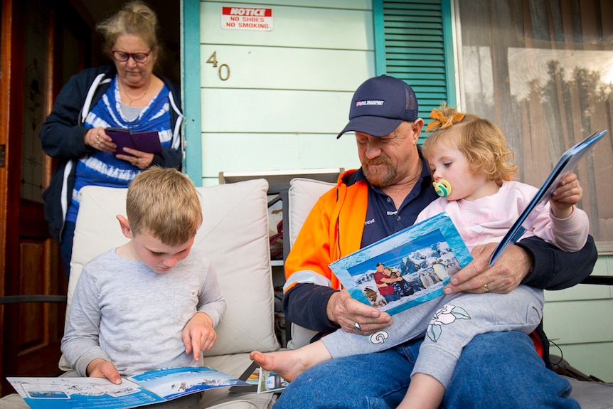 Two children read books with their grandparents.