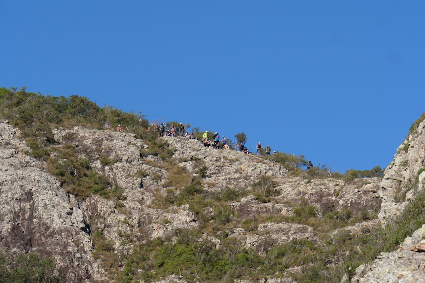 People sitting and walking on scrub and rocks from a distance, blue sky behind.