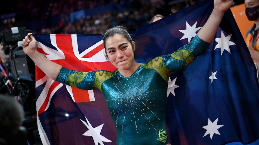 An Australian gymnast tears up as she holds an Australian flag behind her back after clinching a gold medal.