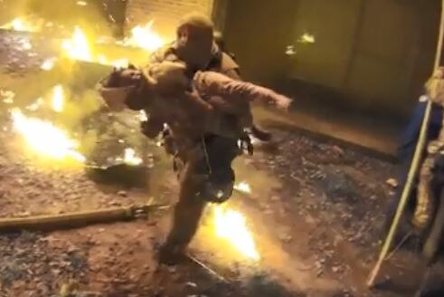 A video still shows a firefighter carrying a young girl through flames