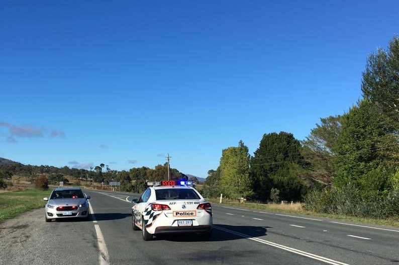 A police vehicle and unmarked car block a single lane highway.