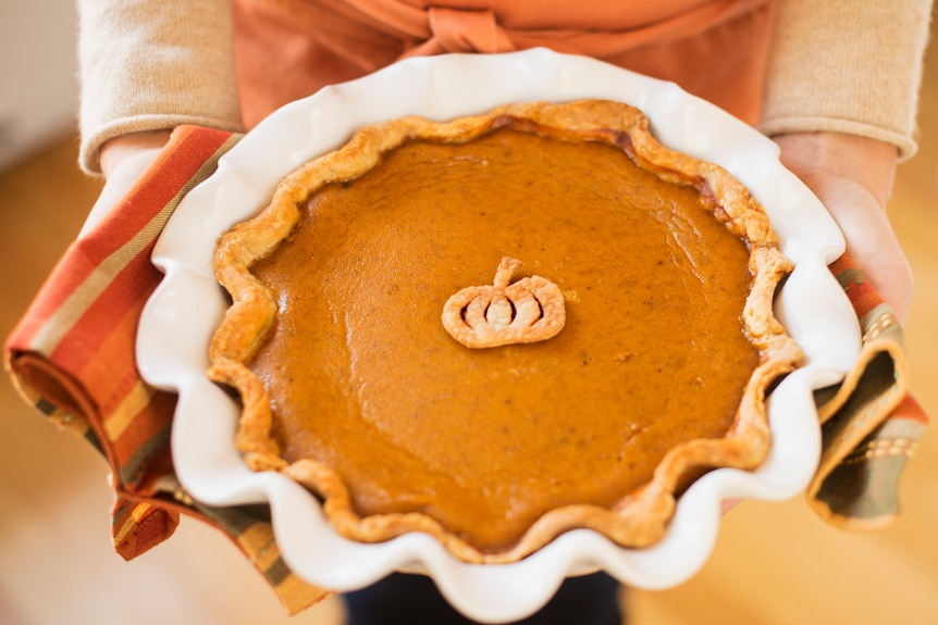 Two hands hold a dish of pumpkin pie
