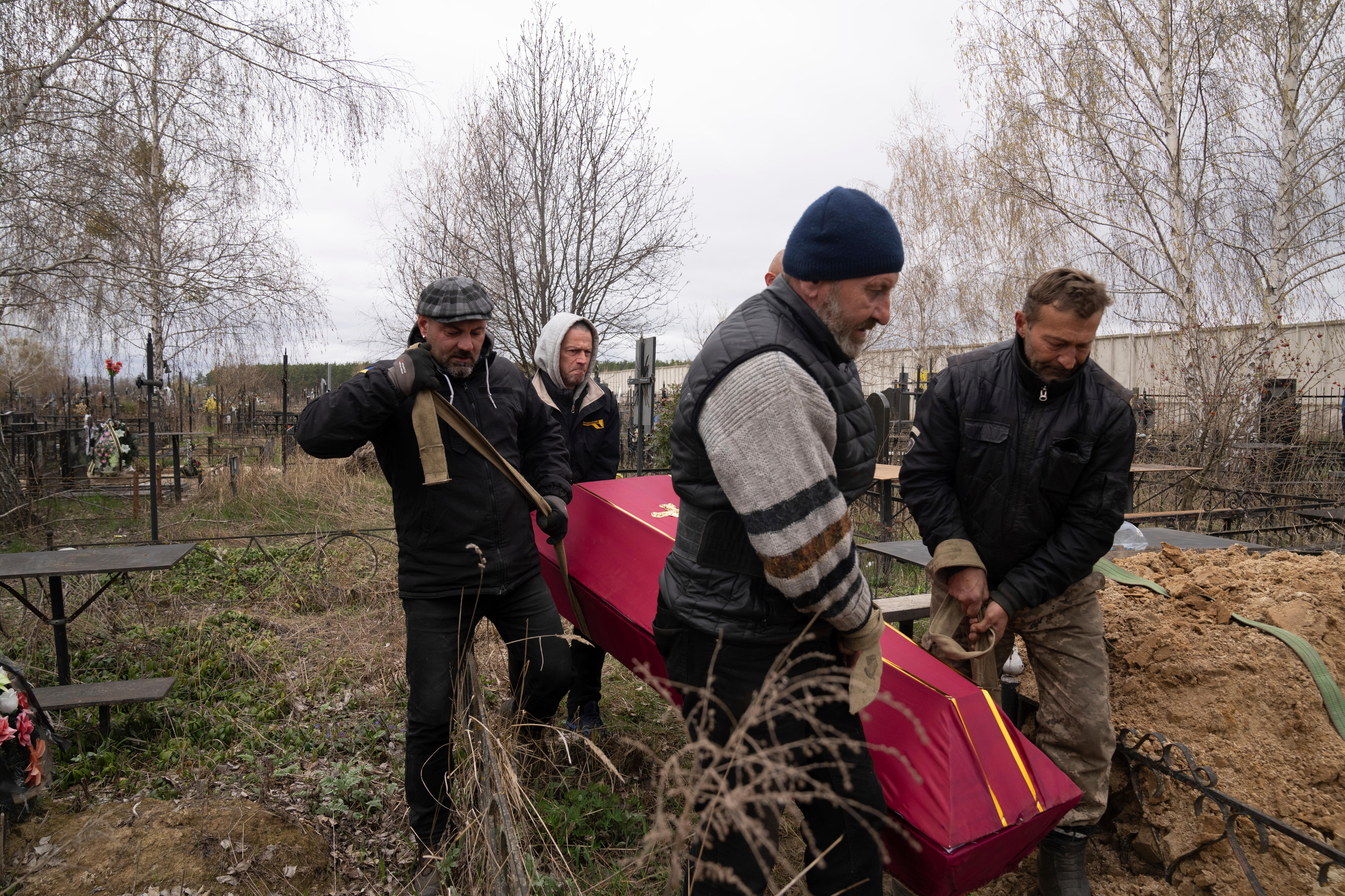 Four men carry a red-coloured coffin through a graveyard on an overcast day