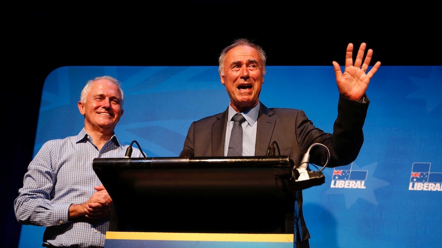 John Alexander speaks at the podium, flanked by Malcolm Turnbull