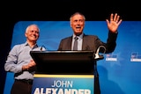 John Alexander speaks at the podium, flanked by Malcolm Turnbull