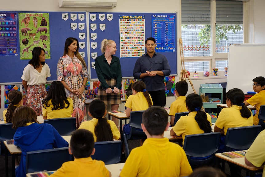 A classroom with four adults speaking to primary school students.