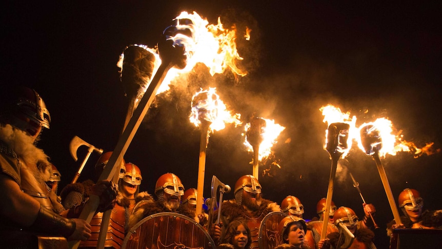 People dressed as Vikings hold flaming torches alight.