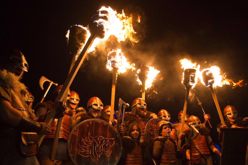 People dressed as Vikings hold flaming torches alight.