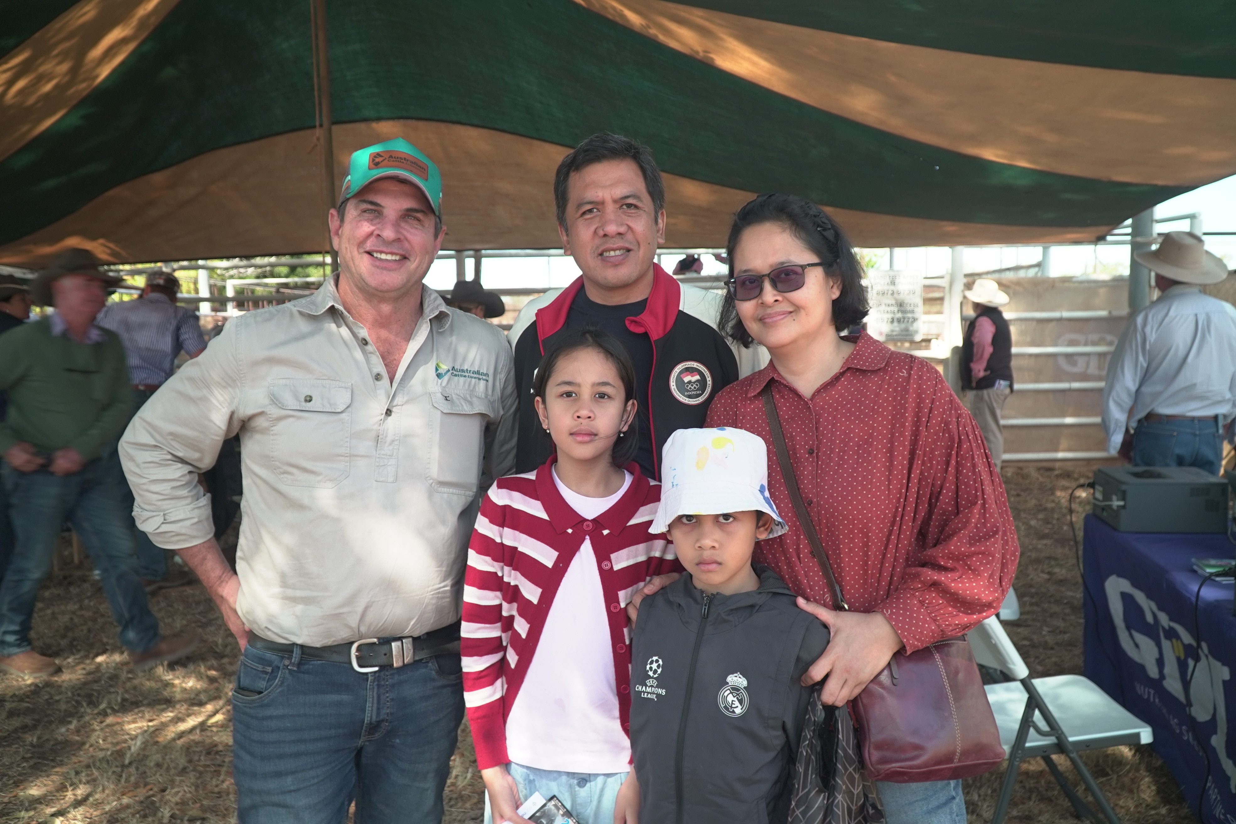 Hombre blanco parado junto a un hombre y una mujer indonesios, una niña y un niño, parados en un pajar, ropa informal.