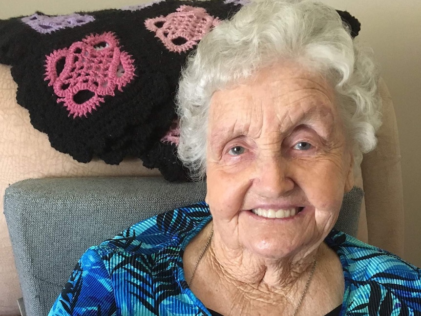 An elderly woman with white hair sitting in a chair, smiling.