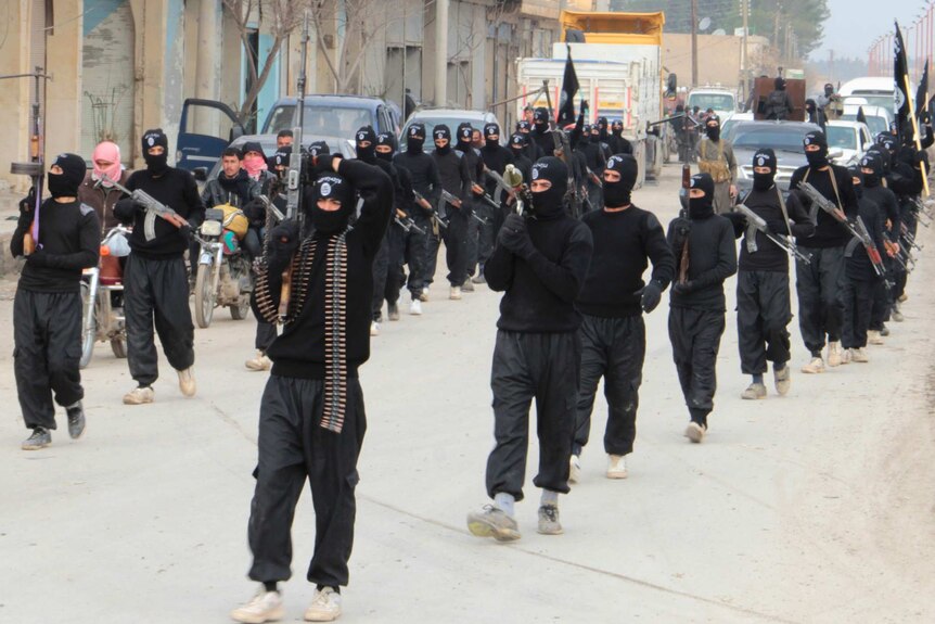 Islamic State fighters wearing all black and face coverings march down a street.
