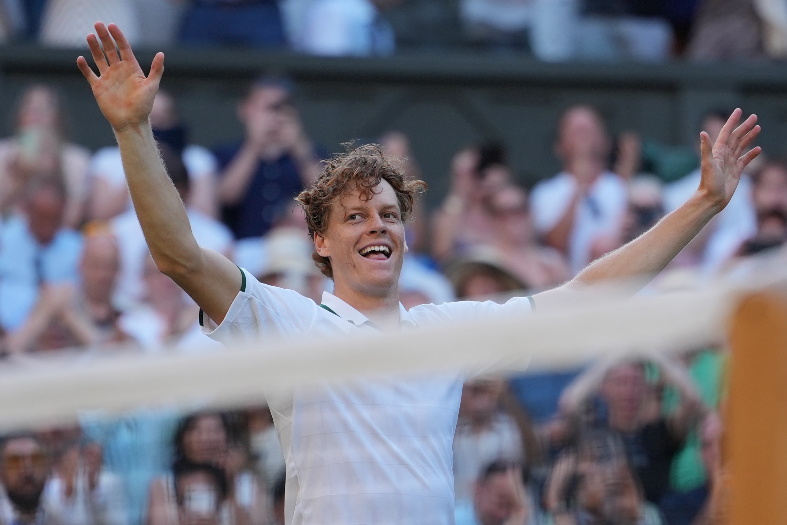 Jannik Sinner smiling with his hands raised above his head.