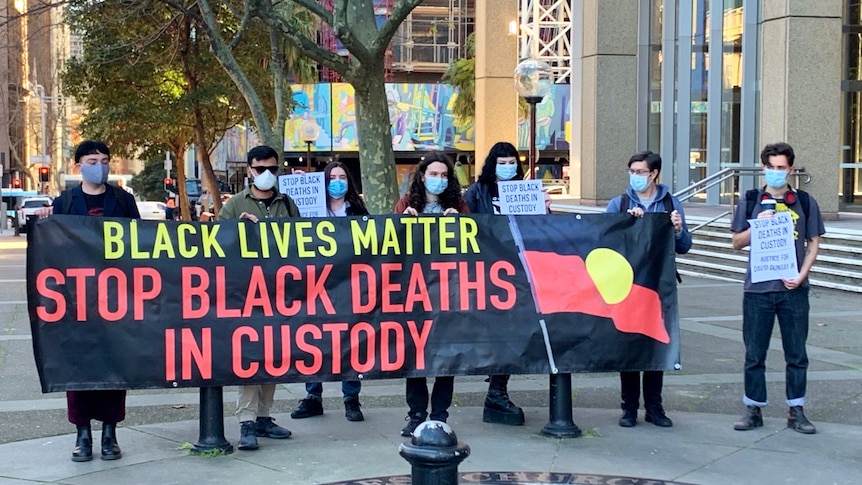 Seven people stand outside the Supreme Court with a banner that reads: "Black Lives Matter. Stop black deaths in custody".