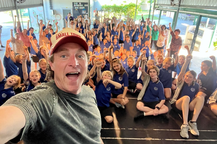 Man's smiling face in foreground with large group of school children in background with fists in the air. 