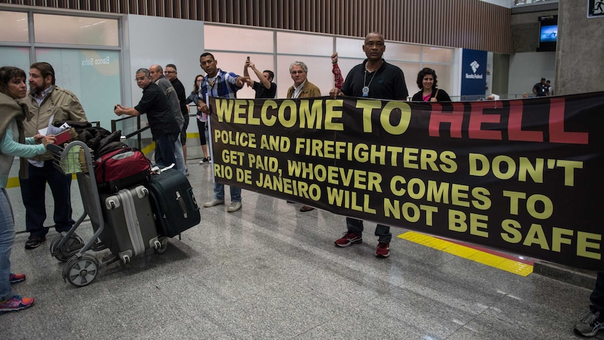 A banner reading "Welcome to Hell" is held up at Rio's airport.