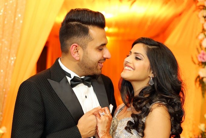 A young couple look into each other's eyes smiling in formal wear at their engagement party.