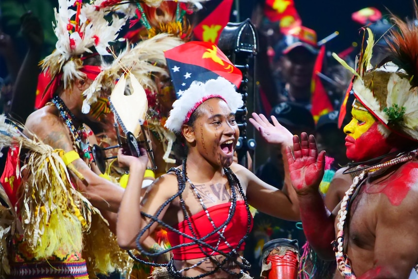 Dancers from Papua New Guinea wearing traditional clothing stand onstage.