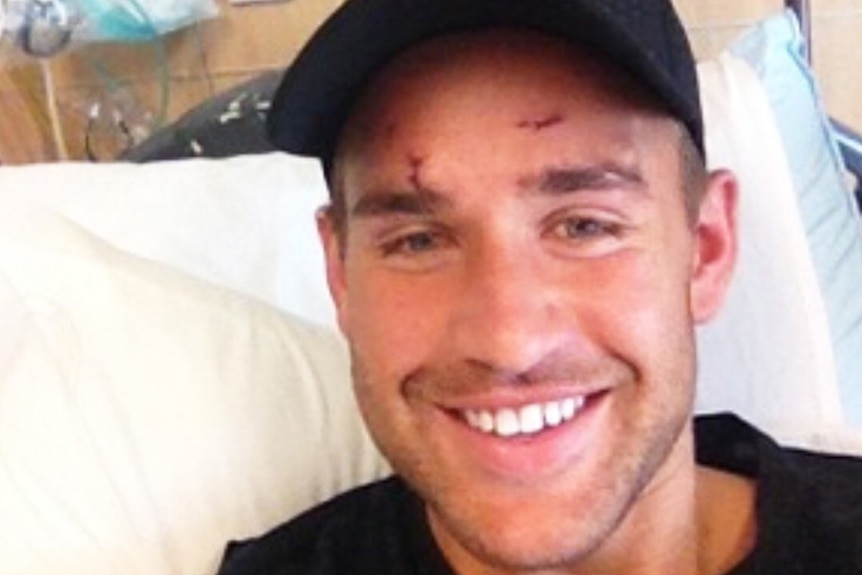 Former Big Brother star Sam Wallace smiles wearing a cap while in hospital bed.