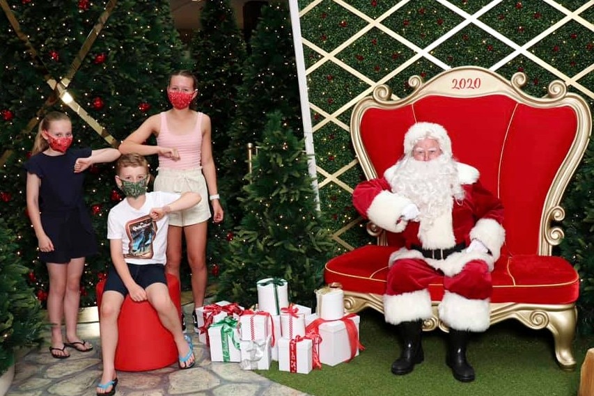 Three kids wearing masks stand apart from a man dressed as Santa.