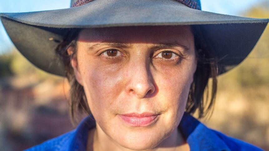 Close up of a woman wearing an Akubra-style hat staring down the lens of the camera.