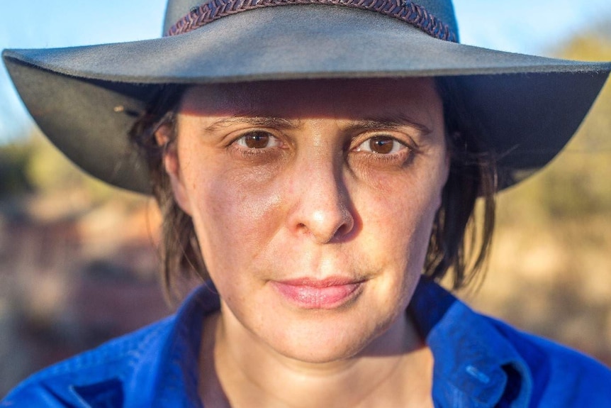 Close up of a woman wearing an Akubra-style hat staring down the lens of the camera.