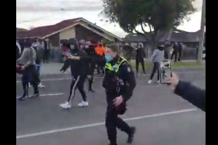 A police officer wearing a surgical mask holds a can of capsicum spray as he walks into a protest in a suburban street.