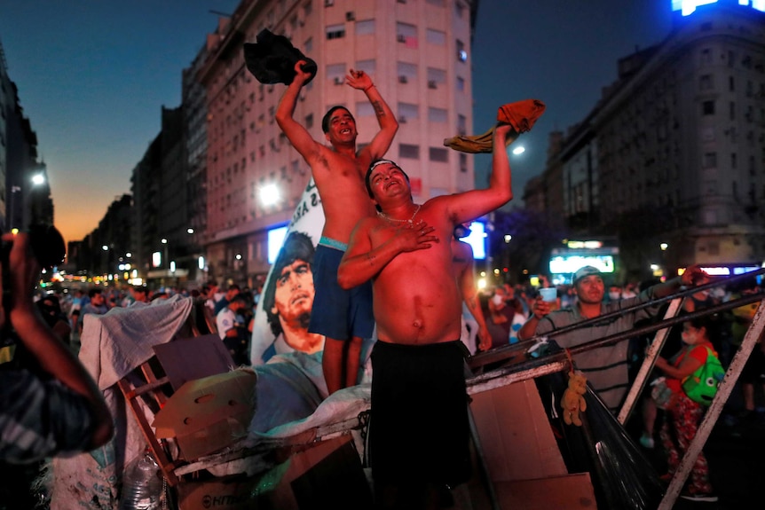 Shirtless men weep while standing on a street in Buenos Aires.