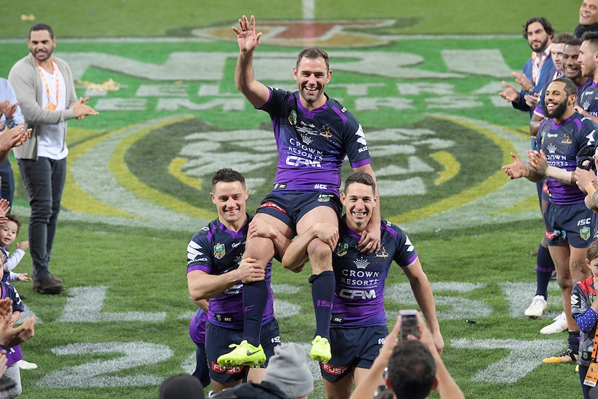 Hooker Cameron Smith of the Storm waves as he is chaired off by Billy Slater of the Storm (right) and Halfback Cooper Cronk.