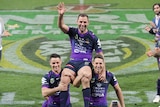 Melbourne's Cameron Smith waves as he is chaired off by Billy Slater and Cooper Cronk.