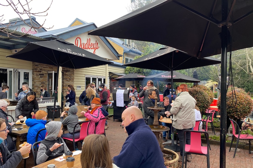 People of different ages sitting in a courtyard with Dudley's sign and drinking and eating.