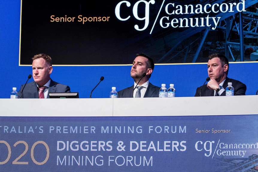 Three mining executives sitting behind a desk at a conference.