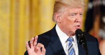 Donald Trump gestures with his right hand while speaking into a microphone in the east room