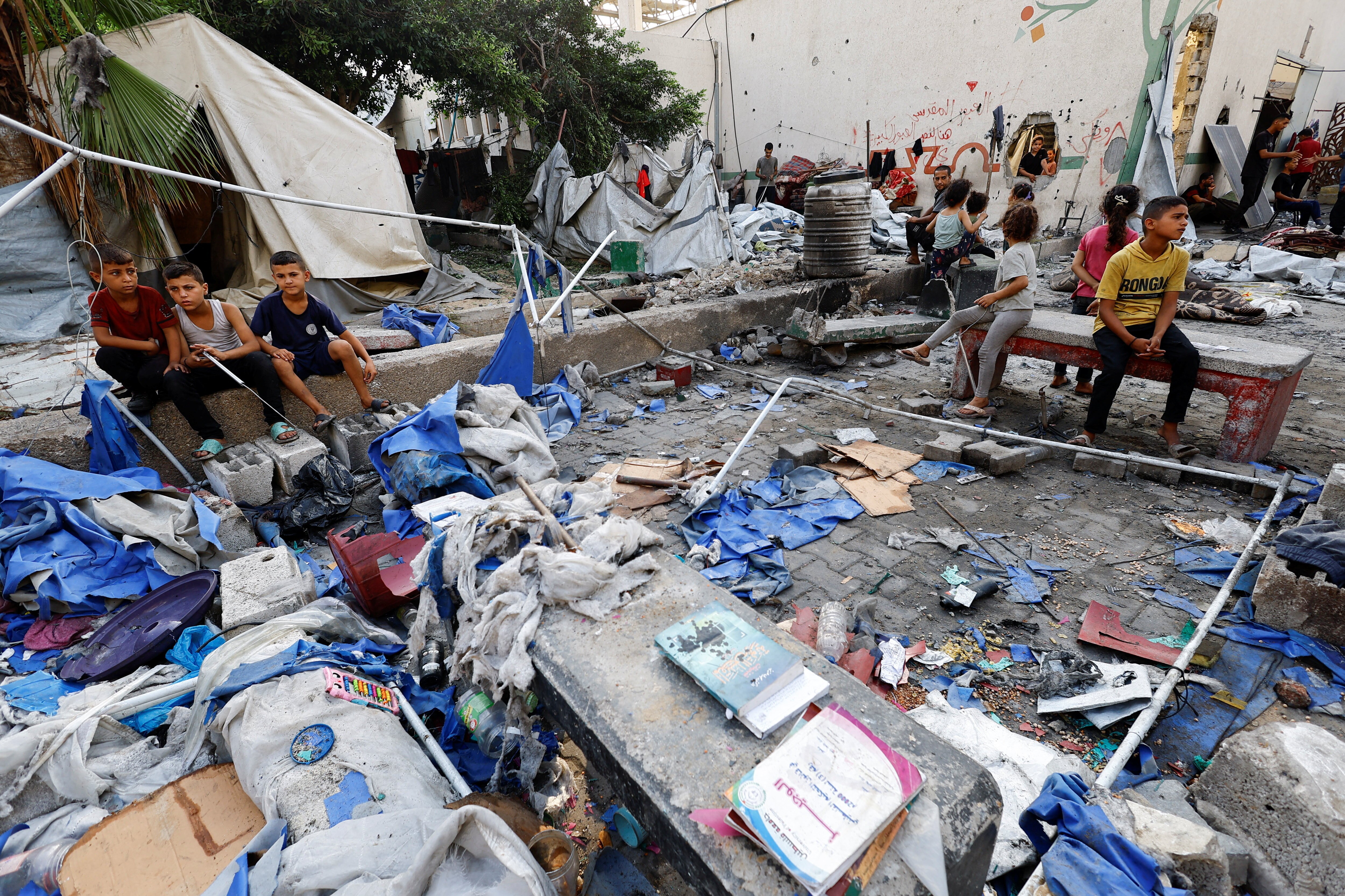 Palestinian children sit at the site of a Friday Israeli strike on a school