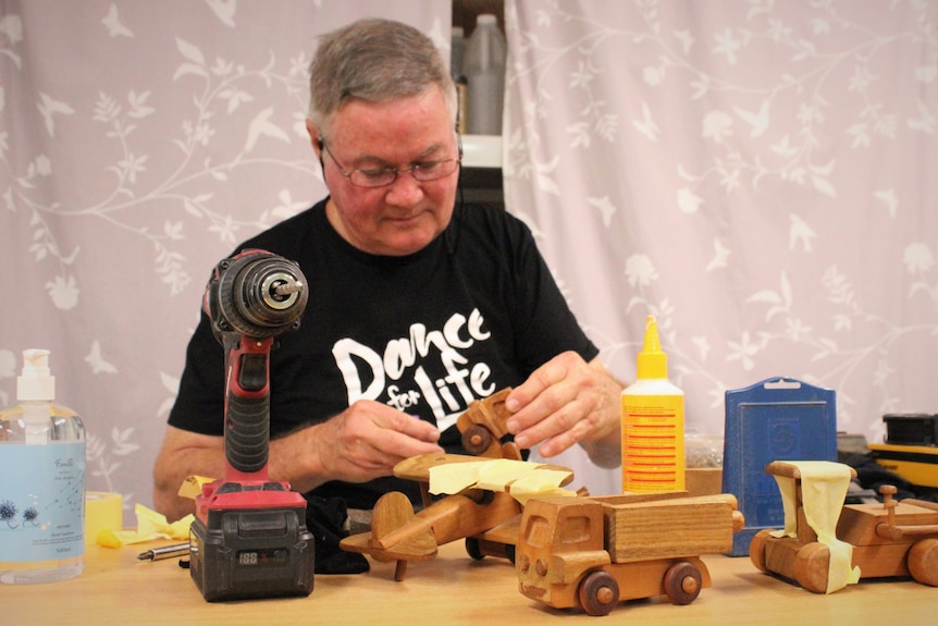 Un homme travaillant sur plusieurs jouets en bois.