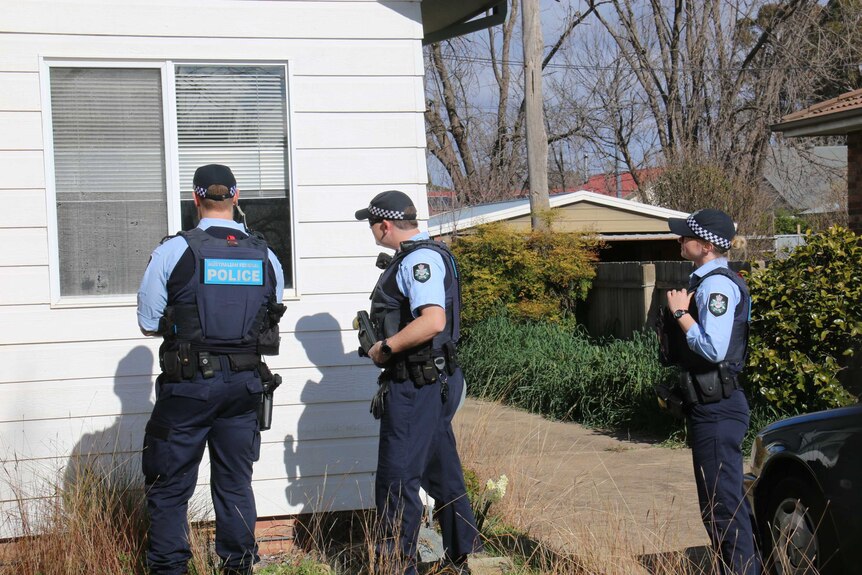 Three police officers look through a window of a home.