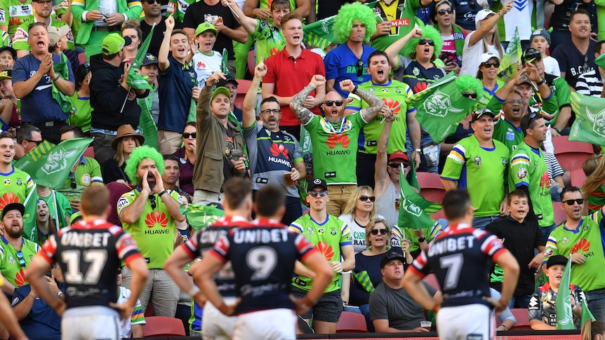 rugby league fans cheering loud while the opposition team is standing with their hand on their hips