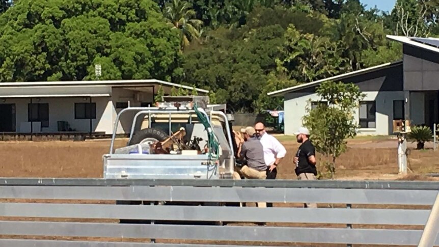 Three men stand around talking to another inside a ute on a rural property