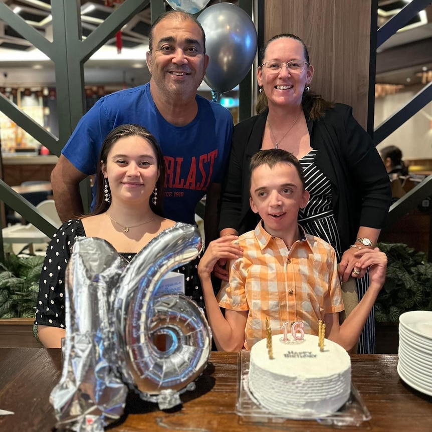 A family at a young man's brithday dinner. He has cake and silver balloon shaped in the number 16. 