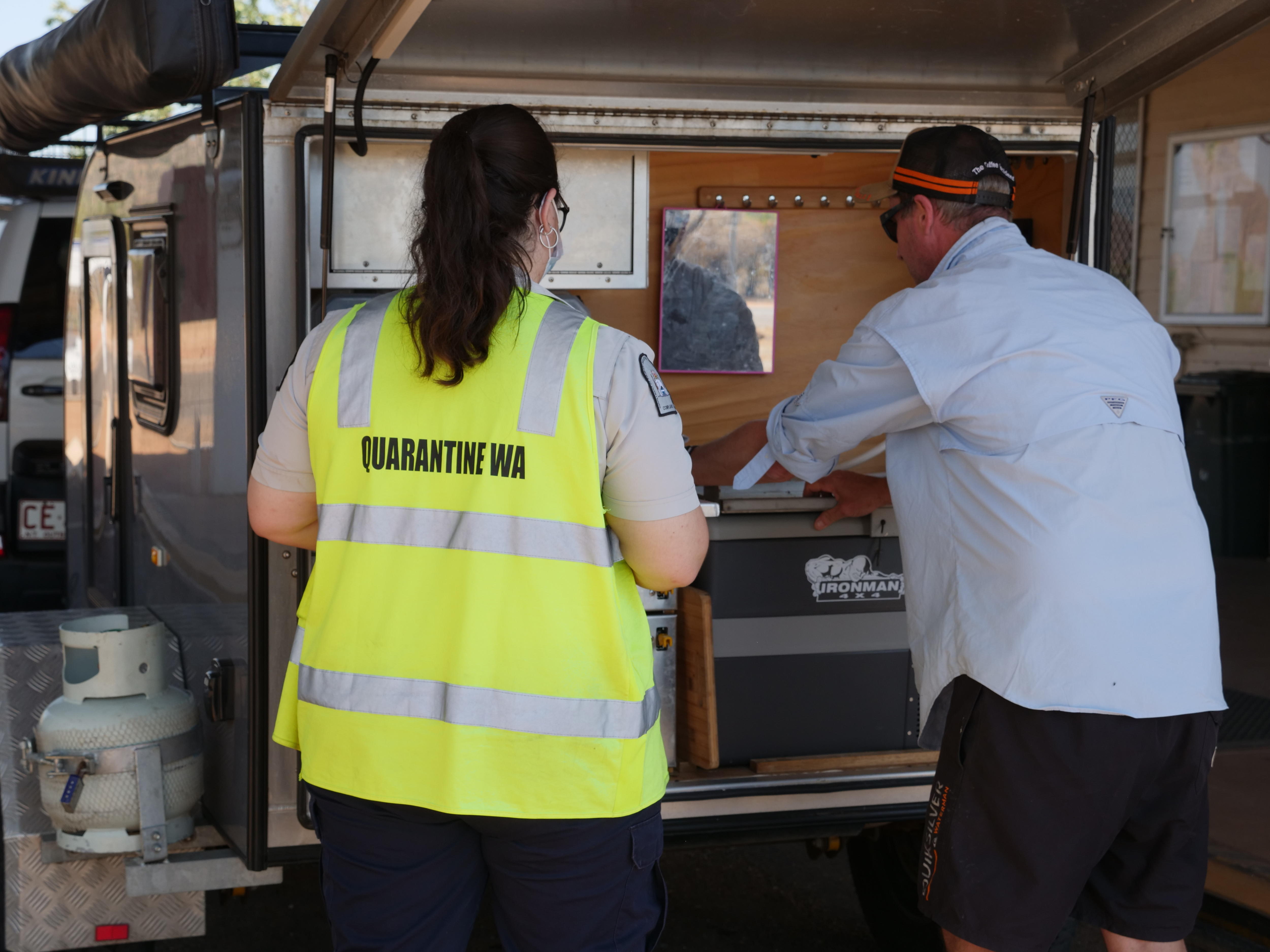 The back of a woman in yellow hi-vis watching a man open an esky in the back of a camper van.