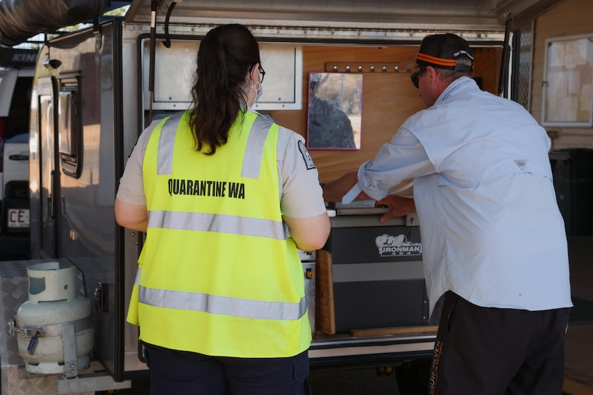 The back of a woman in yellow hi-vis watching a man open an esky in the back of a camper van.