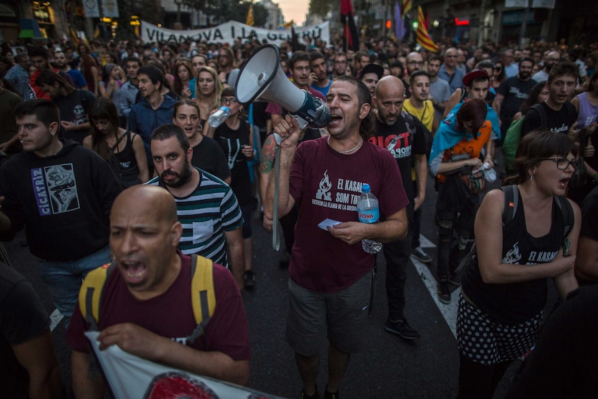 A man yelling into a megaphone leads a large crowd of demonstrators.