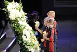 Solemn and uplifting: Children place flowers in a wreath during the service.