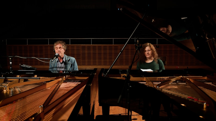 Tim Freedman is seated at a Steinway grand piano with Tamara-Anna Cislowska at another Steinway to his left.