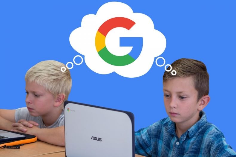 Two boys sit at a desk while using laptop computers